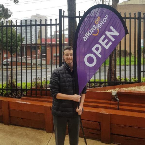 Alkira participant Lachlan holding op shop flag that says Open