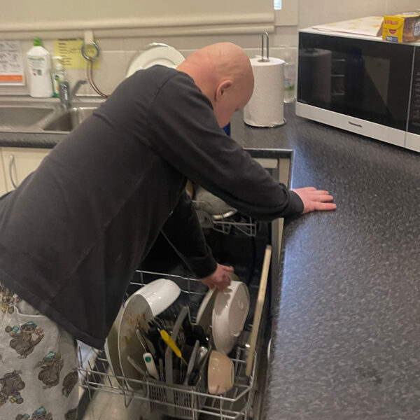 Alkira participant Julian independently stacking the dishwasher in his kitchen.