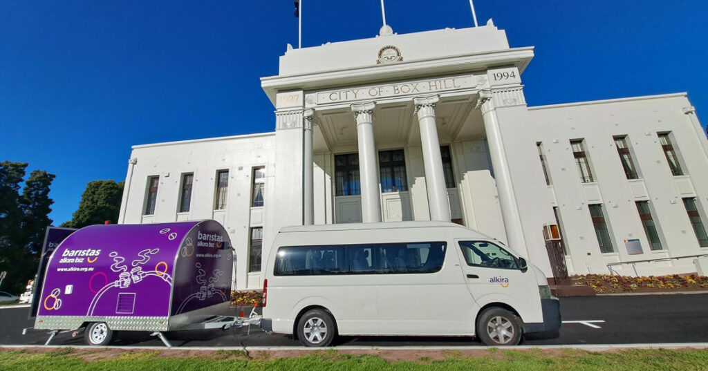 An Alkira bus tows the bright purple AlkiraBiz coffee trailer in front of the Box Hill Town Hall.