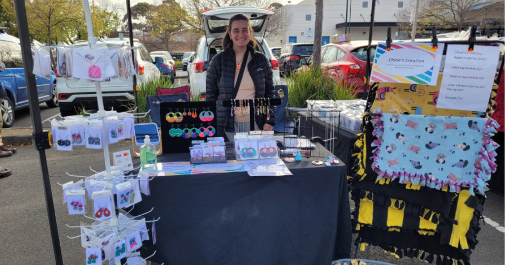Chloe stands at her Chloes Creations stall at Warrandyte Market showing her handmade jewelry and dog blankets.
