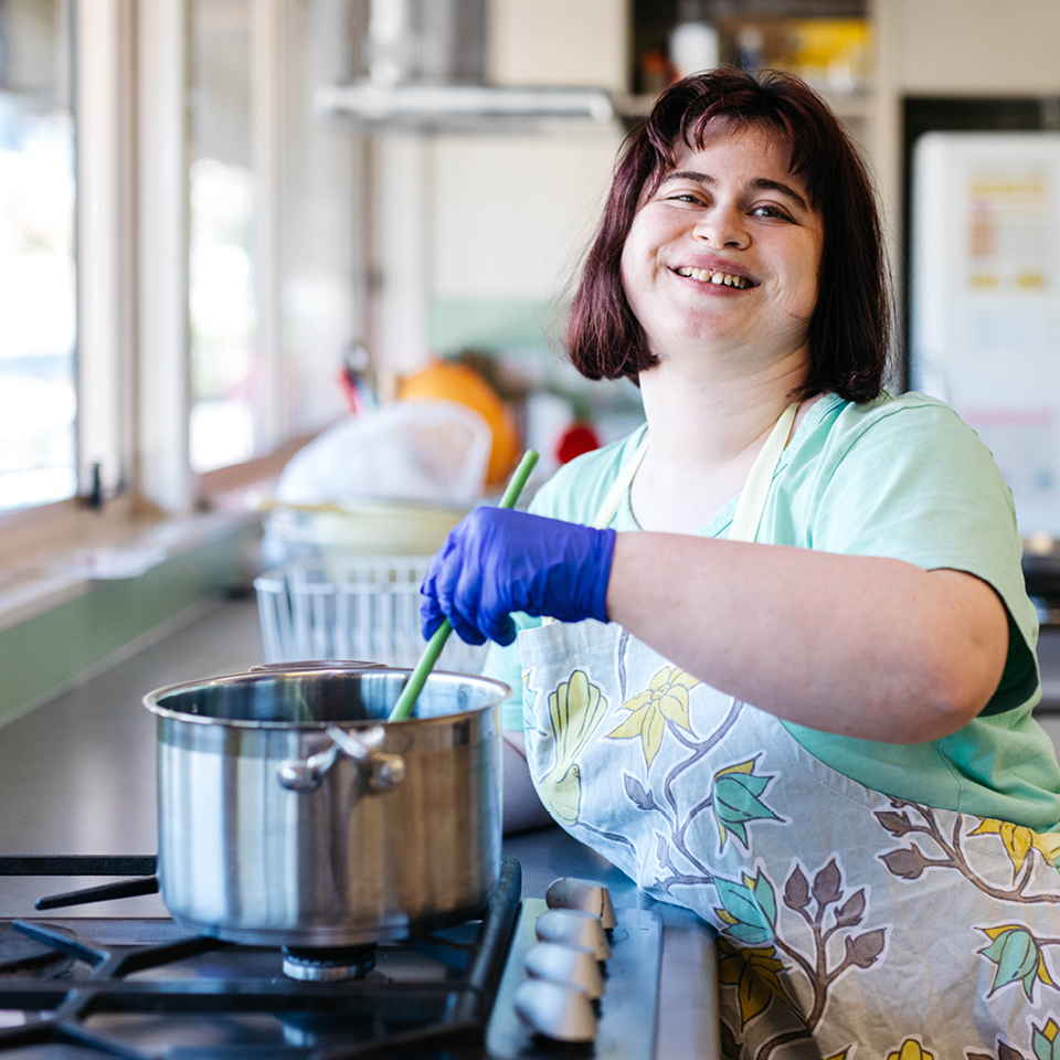 Alkira participant Julia stirs saucepan on stove as a part of her Alkira day programs.