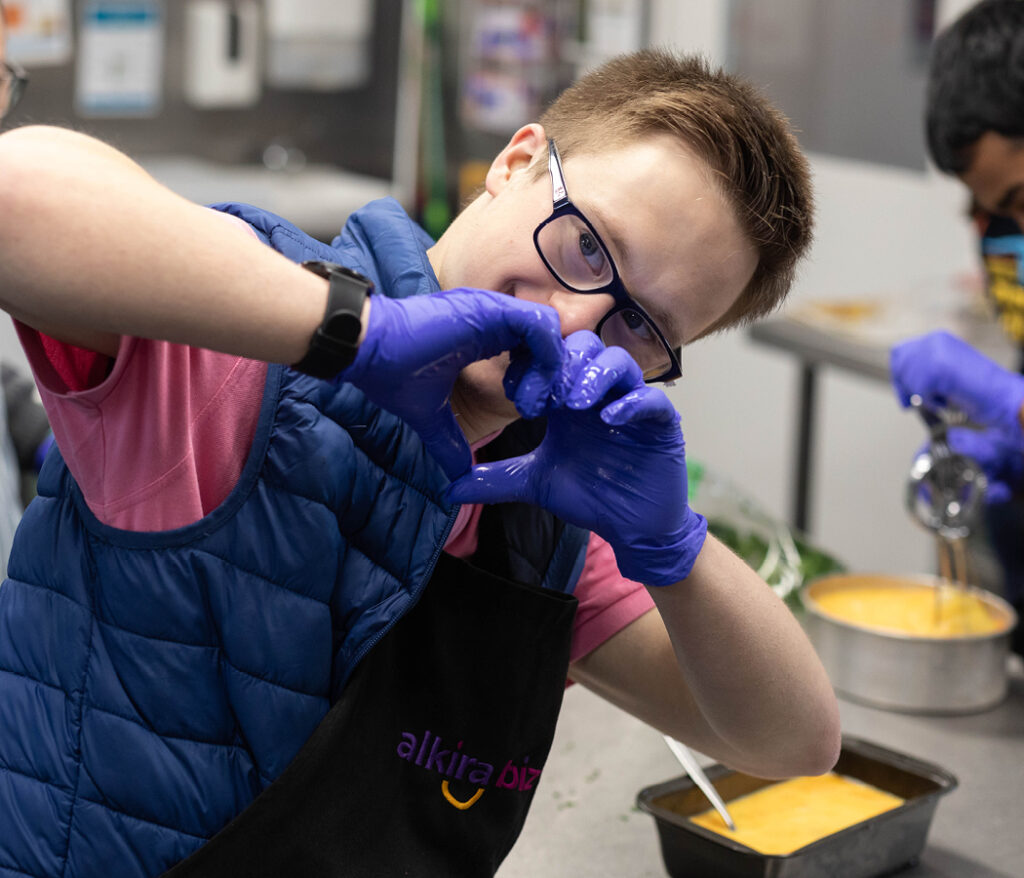 Alkira participant Matthew posing with his hands in the shape of a love heart during his Connections catering day program.