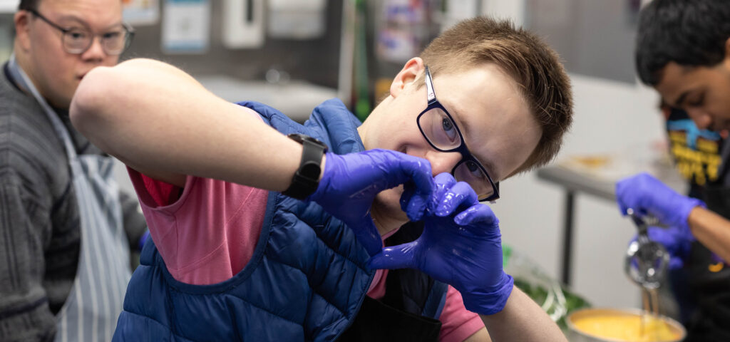 Alkira participant Matthew posing with his hands in the shape of a love heart during his Connections catering day program.