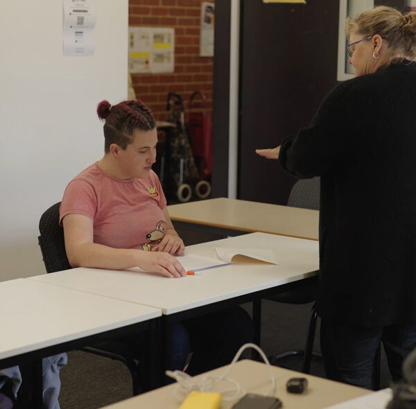 Alkira Networks participant Megan looks at her coursework and listens to her teacher in her classroom.