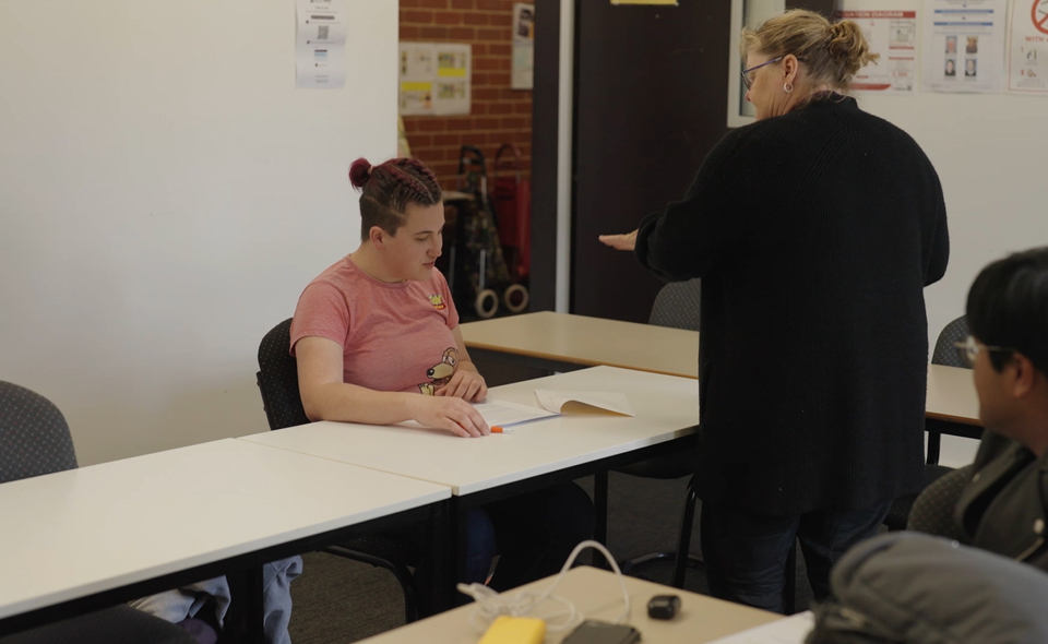Alkira Networks participant Megan looks at her coursework and listens to her teacher in her classroom.