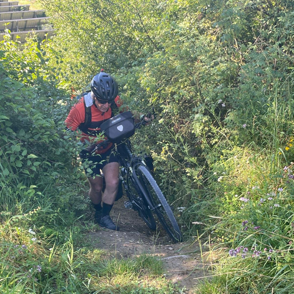 Peter trying hard hiking his bike up a hill amongst trees in Italy.