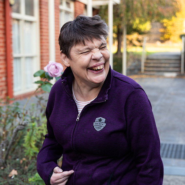 Resident Ruth Walker enjoying herself laughing outside of her home with pink roses in the background.